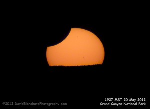 The setting sun -- stil in partial eclipse -- as it dips behind the North Rim of Grand Canyon National Park.