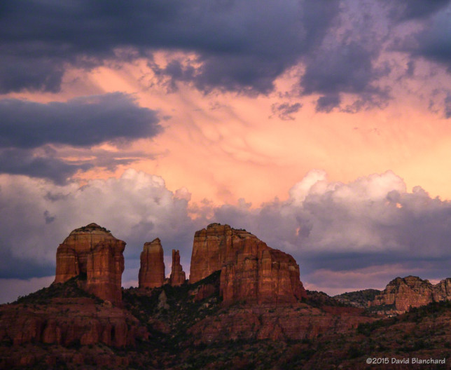 The setting sun lights up the anvil of a thunderstorm behind Cathedral Rock in Sedona, Arizona.